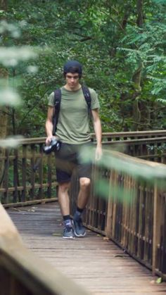 a man walking across a wooden bridge in the woods