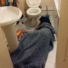 a person laying on the floor in a bathroom under a blue towel next to a toilet