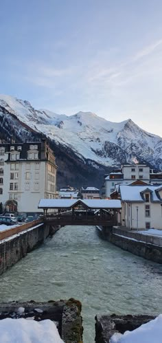 a river running through a snow covered town next to tall mountain range in the distance