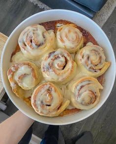 a white bowl filled with cinnamon rolls sitting on top of a wooden table next to a person