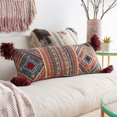 a white couch with two pillows on top of it next to a table and vase