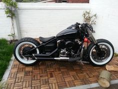 a black motorcycle parked on top of a wooden floor next to a white brick wall