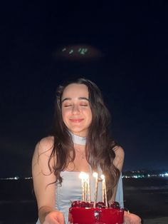 a woman holding a cake with candles on it in front of the ocean at night