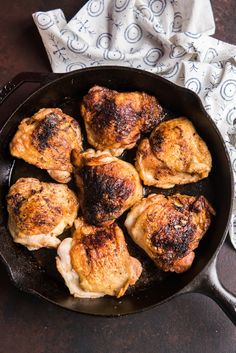 chicken thighs in a cast iron skillet on a wooden table with a napkin and fork