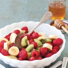 a white bowl filled with sliced kiwis and raspberries next to a honey comb