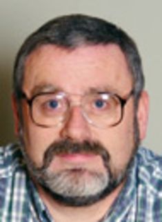 a man wearing glasses and a plaid shirt is looking at the camera with an intense look on his face