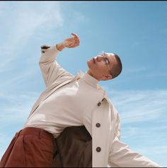 a man in white shirt and brown pants posing for the camera with his hand on his hip