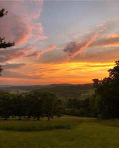 the sun is setting over some trees and hills