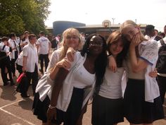 three girls are posing for the camera in front of a group of other people wearing white shirts and black skirts