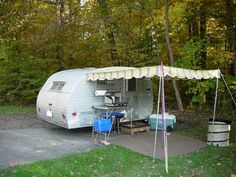 an rv parked in the woods next to a picnic table with chairs and a cooler