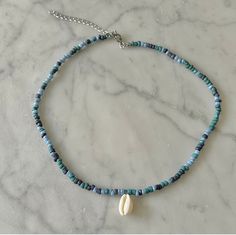 a blue beaded necklace with a white shell hanging from it's side on a marble surface