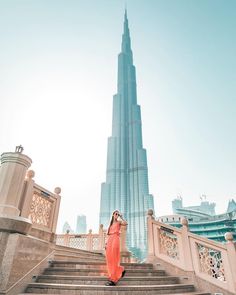 a woman in an orange dress is standing on some stairs with the burj tower in the background