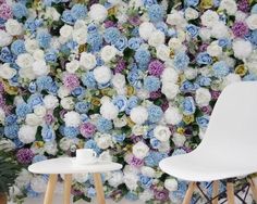 a white chair sitting in front of a wall covered with blue and white flowers