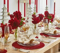 a dining table with red flowers and candles in the background, along with white dishes