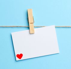 a piece of paper with a red heart on it hanging from a clothesline against a blue background