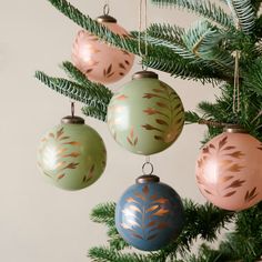 three ornaments hanging from a christmas tree with green leaves on them and gold foiling