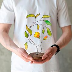 a man holding a small tree with yellow flowers on it's base in his hands