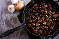 a skillet filled with meatballs and green onions next to garlic on a table