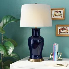 a blue vase lamp sitting on top of a white dresser next to a green wall