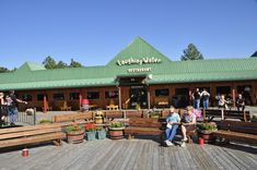 people are sitting on benches in front of a building with green roofing and wooden floors