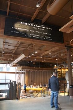 a man standing in the middle of a room with a sign above it that says roastery & tasting room