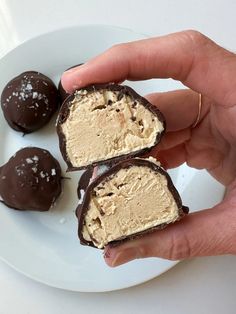 three pieces of chocolate covered ice cream on a white plate with two hands holding one