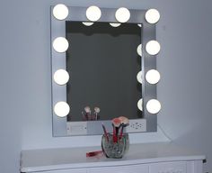 a vanity mirror with lights on top of it next to a vase filled with makeup brushes