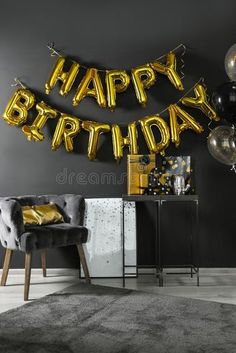 a birthday party with gold foil balloons and black chairs in front of a gray wall