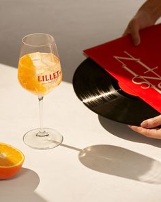 a person holding an orange next to a vinyl record and a glass of wine on a table