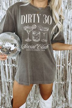 a woman holding a disco ball in front of a silver tinsel backdrop with the words dirty 30 on it