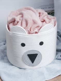 a white basket with a bear face on the inside and a pink towel in it