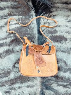 This genuine leather saddle purse is an absolute must-have! It's modeled after a saddle for a truly unique design. Plus, it features an adjustable shoulder strap so you can adjust the fit. An out-of-the-box way to accessorize with flair! Tooled Leather Saddle Purse: Measures appx. 10" x 9" x 4". Crafted of genuine leather. Available in tan & brown. Comes with adjustable strap. Made in Mexico. Weight: 2 lbs. Visit us on Facebook for inspirational ideas on decorating any space. Don't forget to fol Saddle Bag With Detachable Strap For Daily Use, Western Style Shoulder Bag For Everyday, Travel Saddle Bag With Adjustable Strap, Daily Use Saddle Bag With Adjustable Strap, Saddle Bag With Removable Pouch, Western Style Crossbody Shoulder Bag For Travel, Saddle Bag With Removable Pouch For Daily Use, Adjustable Leather Crossbody Bag, Everyday Saddle Satchel With Removable Pouch