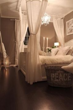 a bed with white sheets and curtains next to a chandelier in a bedroom