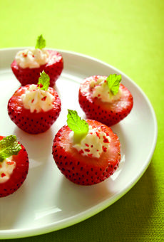 four strawberries with whipped cream and mint leaves on a white plate against a green background