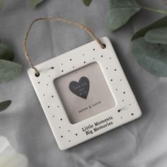 a small white frame with a heart hanging from it's side on a table