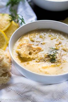 a white bowl filled with soup next to slices of lemon and bread on a table