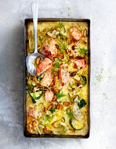 a square casserole dish with chicken, vegetables and sauce on the side next to a spoon