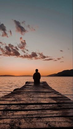 a person sitting on a dock watching the sunset