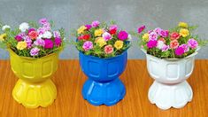 three colorful flower pots sitting on top of a wooden table