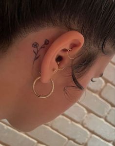 a woman's ear has a small flower tattoo on it