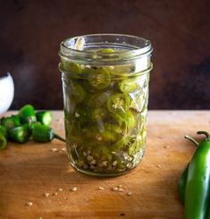 a jar filled with pickles sitting on top of a wooden table next to green peppers