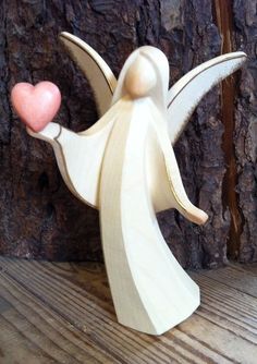 a small wooden angel holding a pink heart