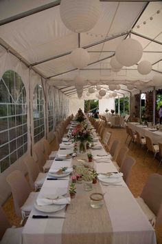 a long table set up with white plates and napkins for an outdoor function hall