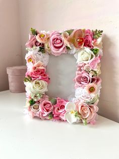 a white frame with pink and yellow flowers on it is sitting on a table next to a wall