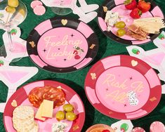 pink plates with writing on them are sitting on a green tablecloth covered in food