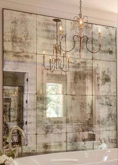 a bath tub sitting under a bathroom mirror next to a sink and chandelier