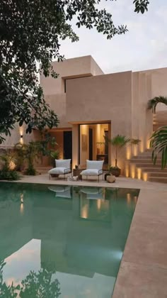 an outdoor swimming pool surrounded by greenery and lights at dusk, with lounge chairs on either side