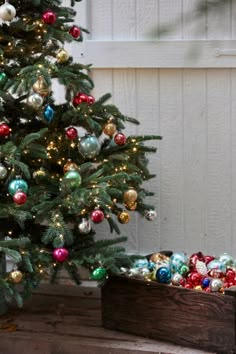 a small christmas tree with ornaments on it in front of a white wall and wooden box