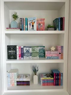 a white book shelf filled with lots of books next to a vase and potted plant