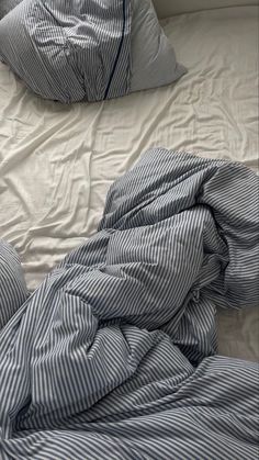 an unmade bed with blue and white striped comforter on top of it, next to two pillows